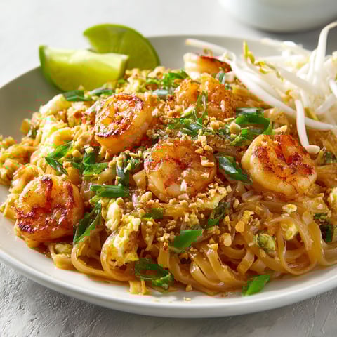 Un Pad thaï aux crevettes avec des légumes verts et noix de coco, posé sur une table.
