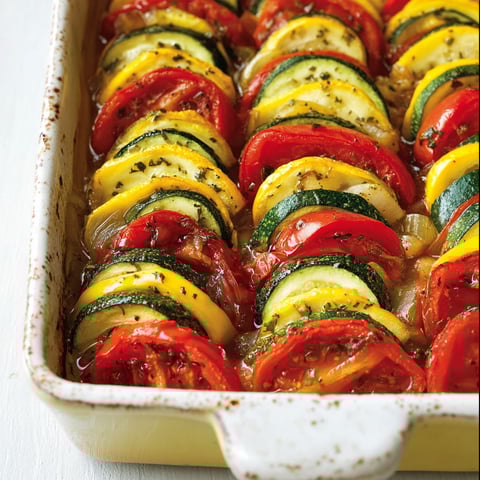 On voit un tian de courgettes présentant joliment ses couleurs dans un plat transparent.