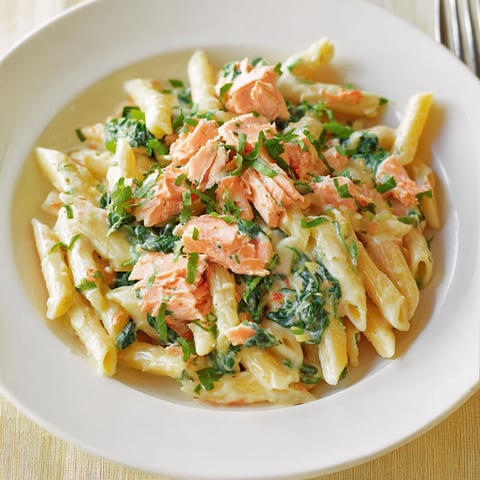 Dans une assiette, des pâtes crémeuses au saumon avec une touche de coriandre et de légumes verts.