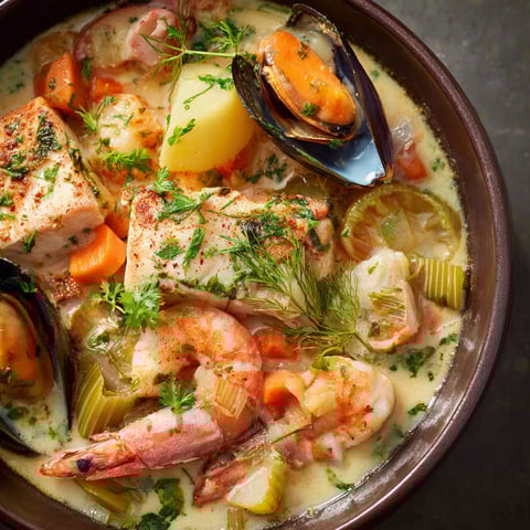 Une assiette de pot-au-feu de la mer garnie de moules, carottes et légumes variés.