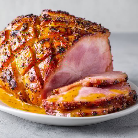 Belle tranche de jambon de Noël bien dorée, nappée de miel et moutarde, placée sur un plateau dédié à la fête.