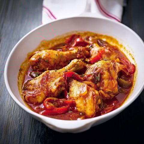 Une assiette de poulet basquaise, entourée de tomates, oignons et épinards, déposée sur une table.