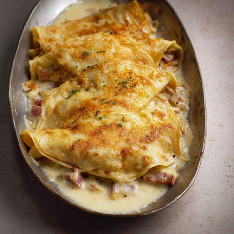Une grande crêpe bien garnie à la béchamel et au jambon posée sur un joli plat argenté.