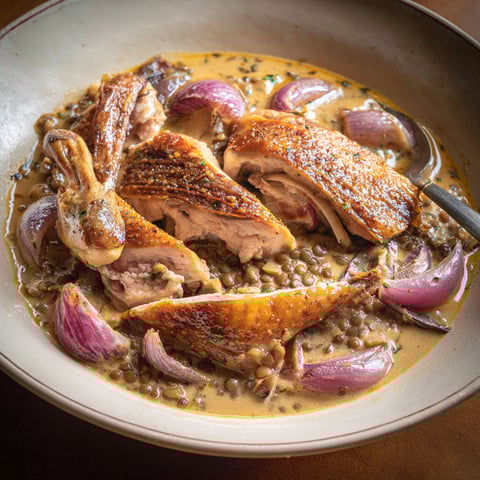 Sur une table, une assiette de pintade à l’auvergnate accompagnée de légumes colorés et d’herbes fraîches.